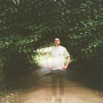 Lazerbeak, guy in white t-shirt surrounded by green leaves.