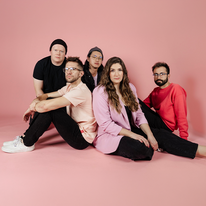 Maria & the Coins, group of five adults sitting together and posing on a pink background.