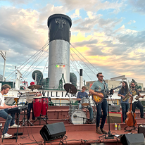 band of six guys performing on top of a large ship.