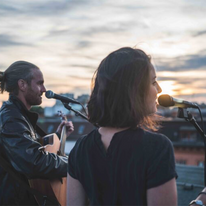 Water Cat band, man and woman singing in mics together outside.