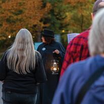 cloaked tour guide holding a lit lantern and leading group of guests on a lantern tour.