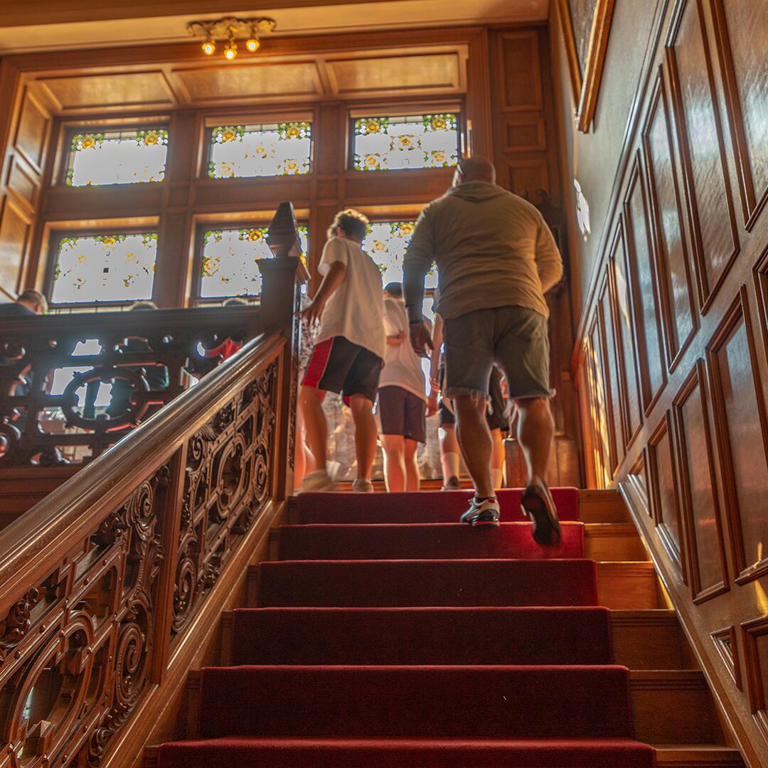Family climbing up the main red staircase of Glensheen.