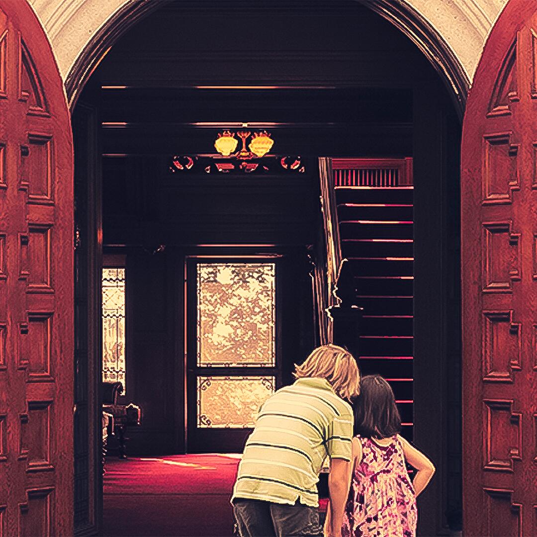 large open doors to the mansion entrance, two kids peering in to see the grand foyer