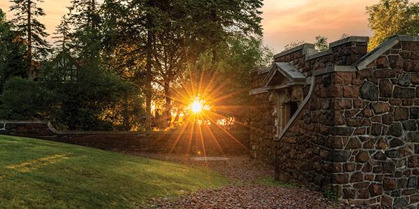 sun peering through trees next to the stone boathouse.
