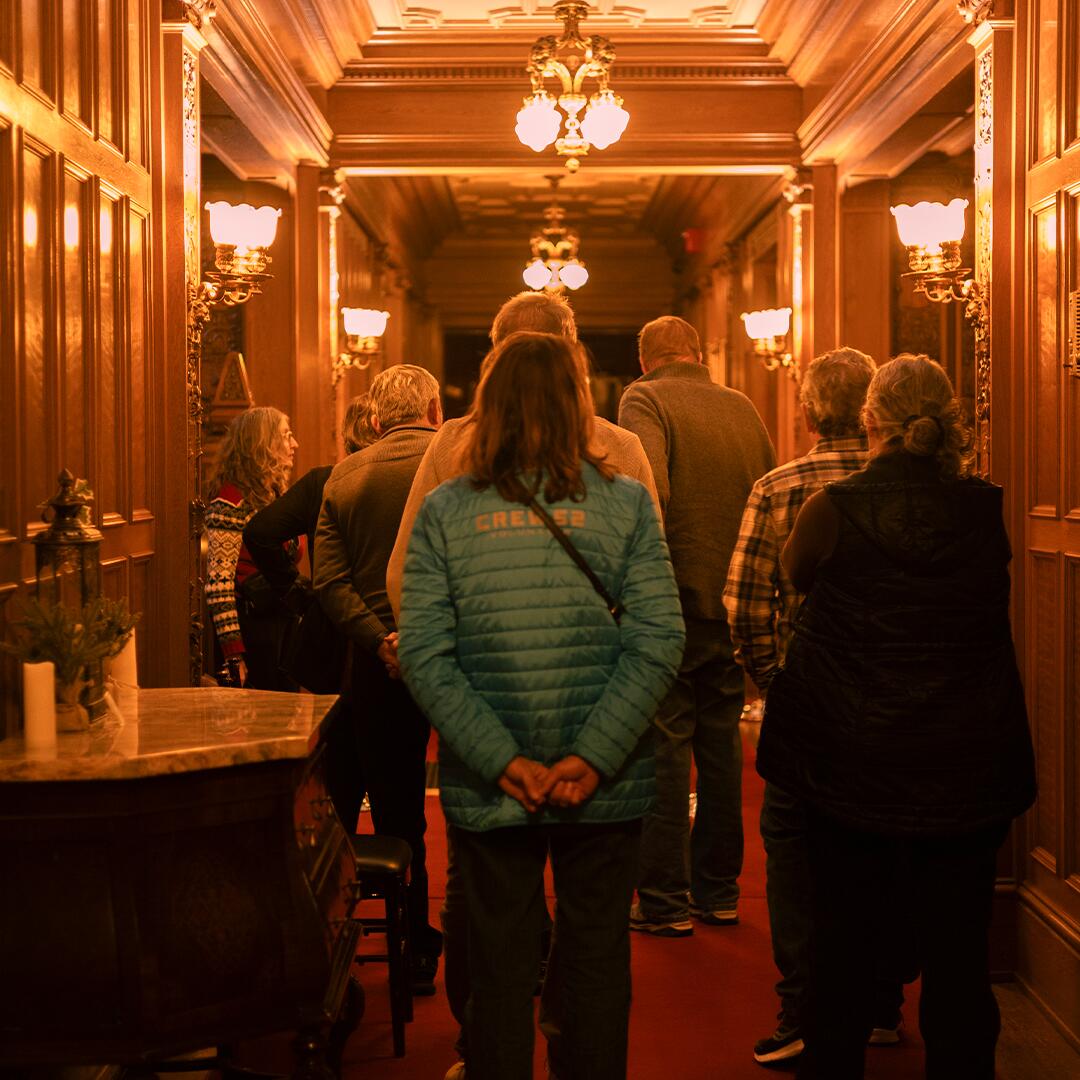 Group of mature adults in wooden paneled main hall of Glensheen.
