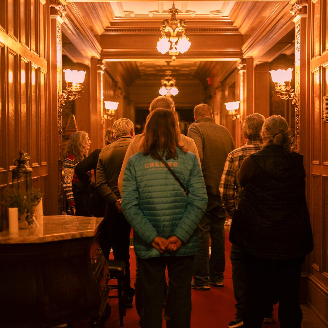 Group of mature adults looking around at the main wood paneled hallways at Glensheen.