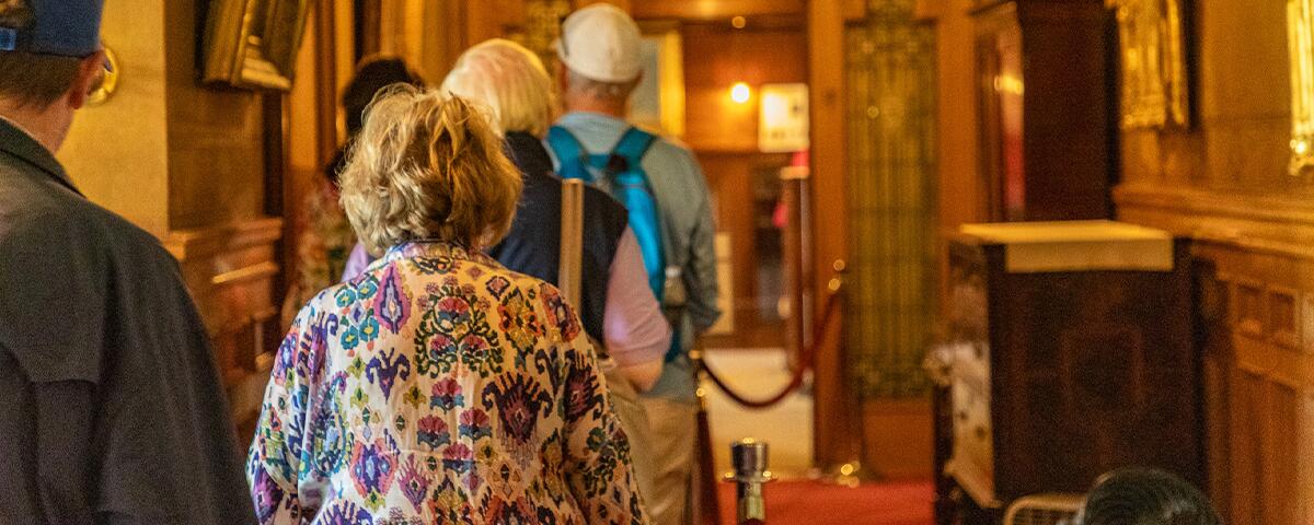 Group of mature adults in wooden paneled main hall of Glensheen.
