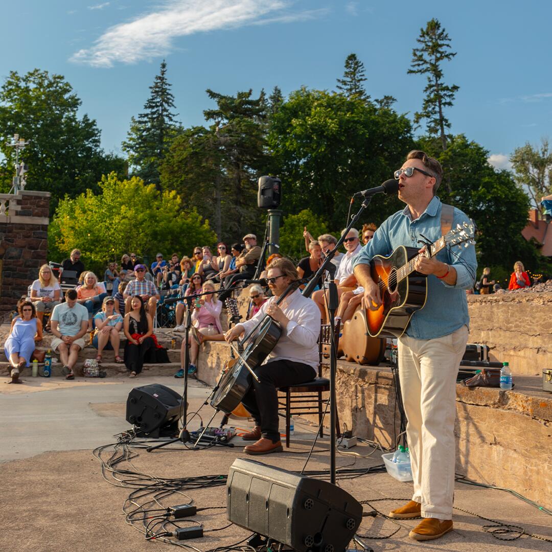 musician performing with guitar and crowd of guests watching around him.