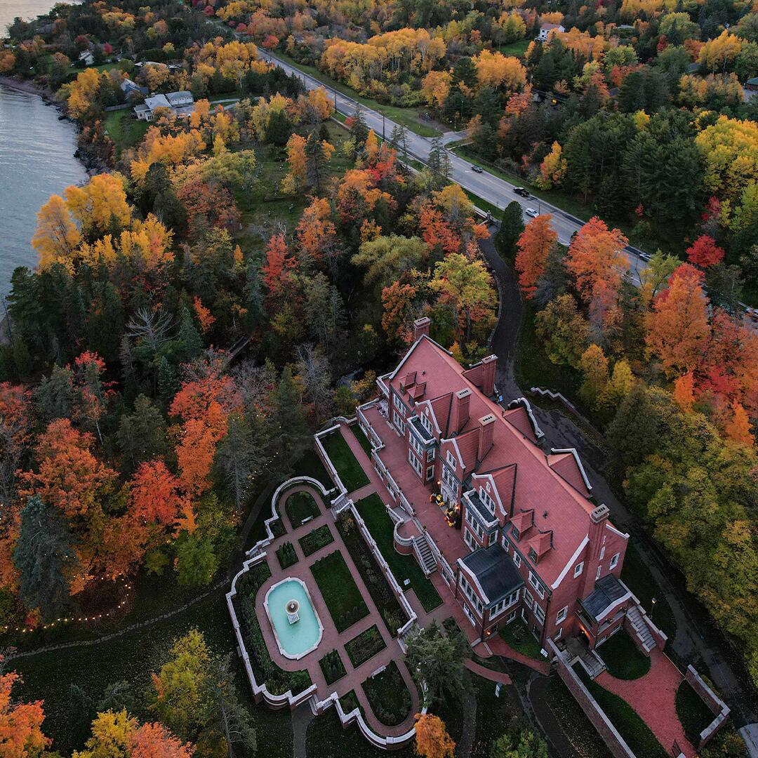 Glensheen mansion viewed from above with road behind it, surrounded by colorful trees in fall.