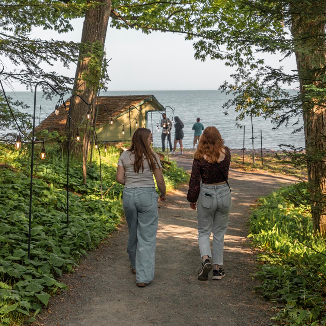 Two women walking along a gravel path with trees and plants around them.