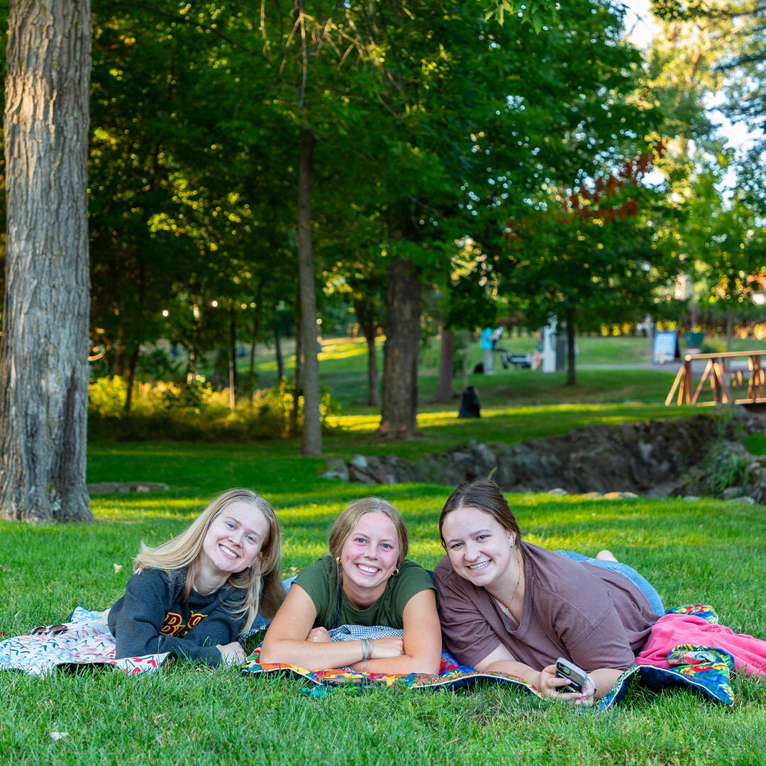 Three college students laying in the grass on blankets.