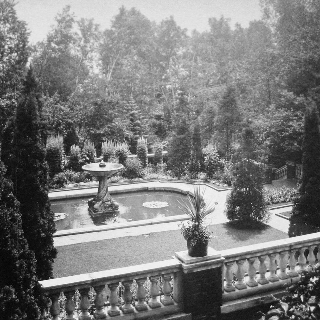 stone and brick terrace overlooking a large marble fountain, surrounded by pruned trees.