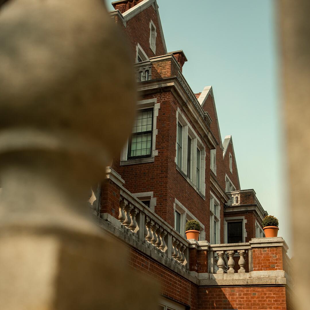 side of a large brick building seen through stone fencing.