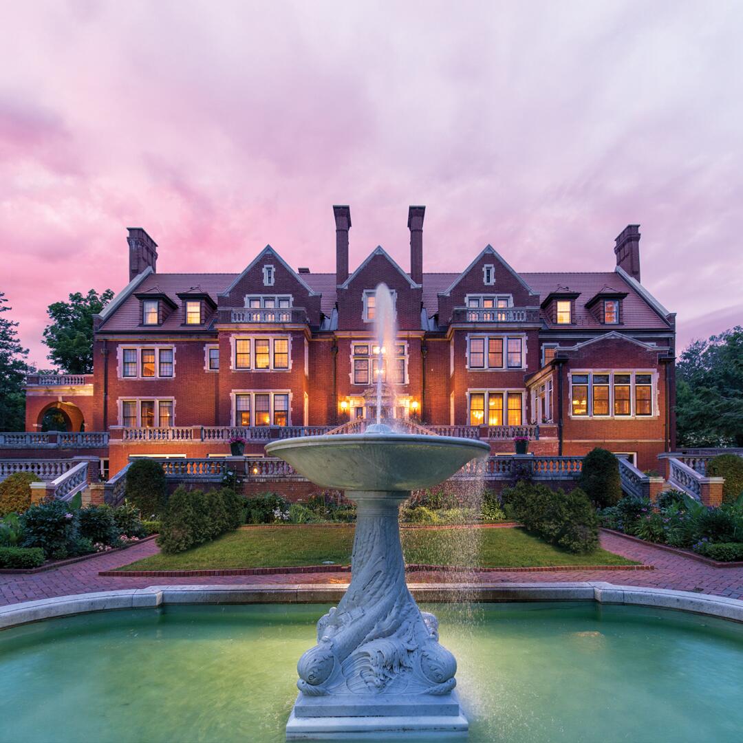 brick exterior of Glensheen with fountain in front with colorful sunset sky background.