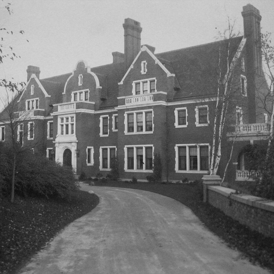 The front of a large brick mansion along a winding paved path.