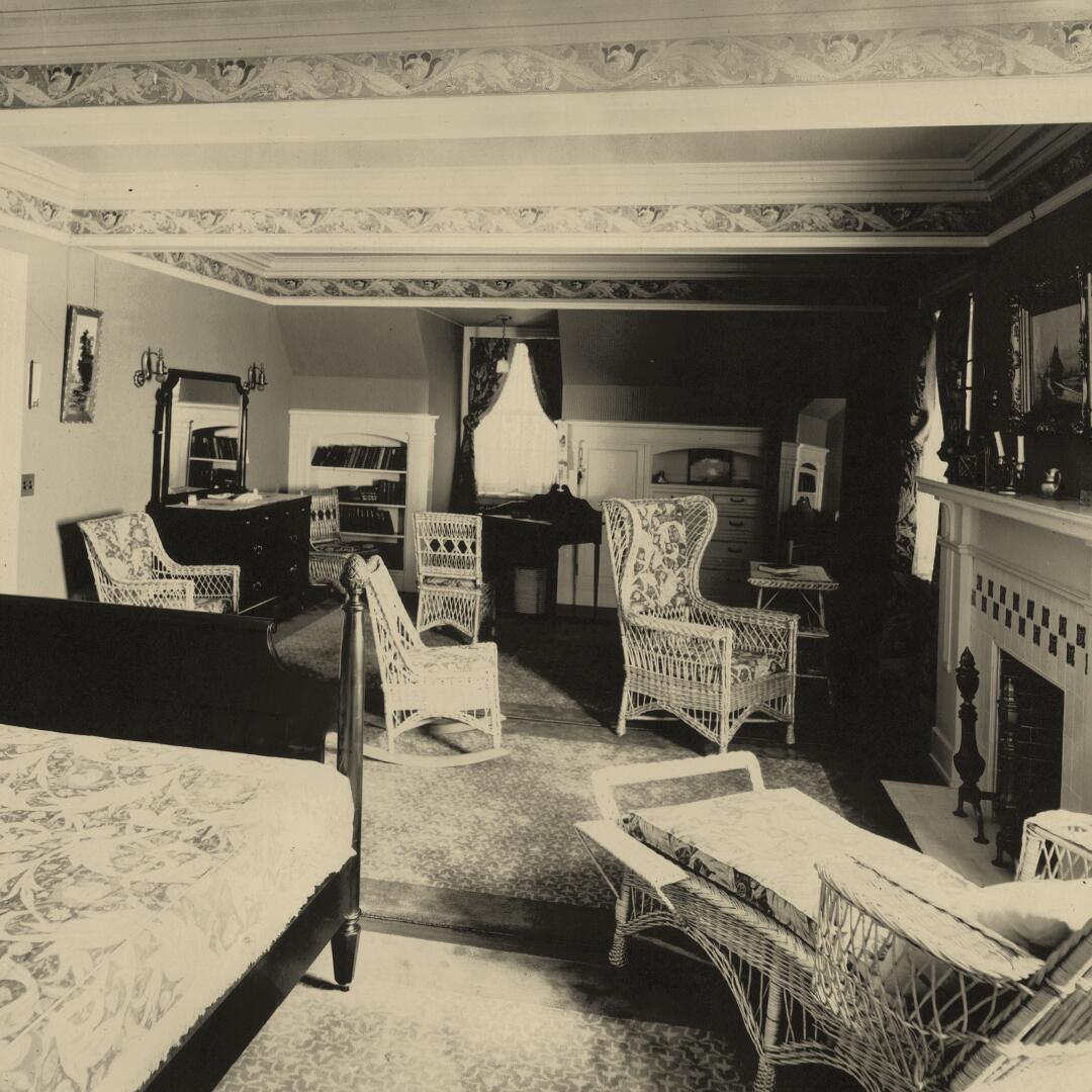bed and wicker furnishings with a fireplace, dresser, desk, and mirror in a large open bedroom
