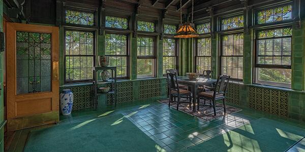 green tiled room with oak leaf stained glass windows, a wooden table, and hanging light fixture.