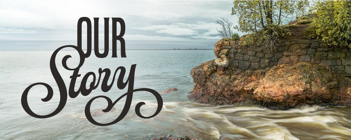 a small stone cliff with trees and a stream of water rushing into Lake Superior: Reads Our Story.