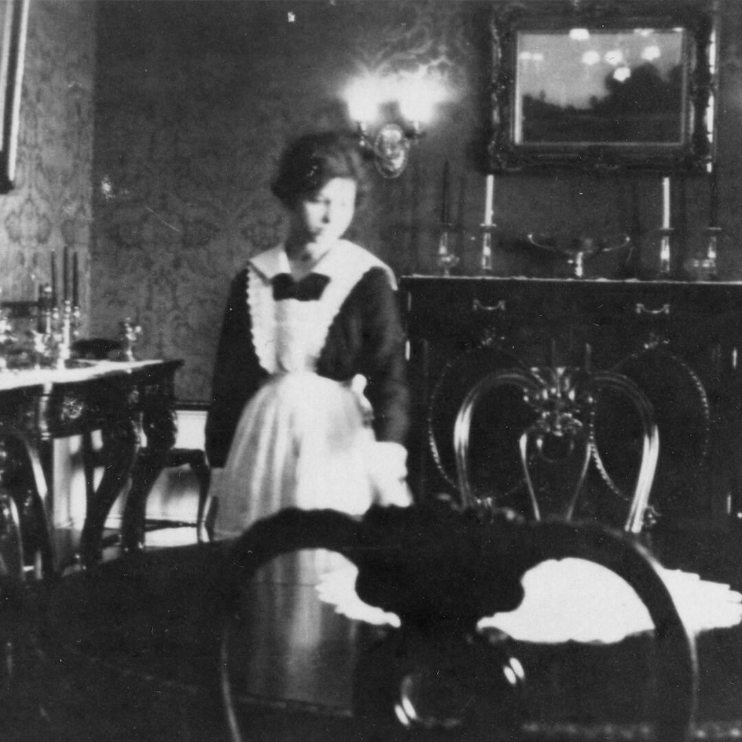 a housemaid in uniform standing in the formal dining room.