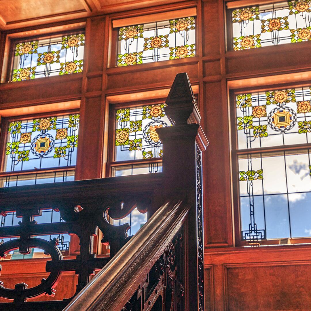 large wooden paneled stained glass windows behind wooden stair railing.