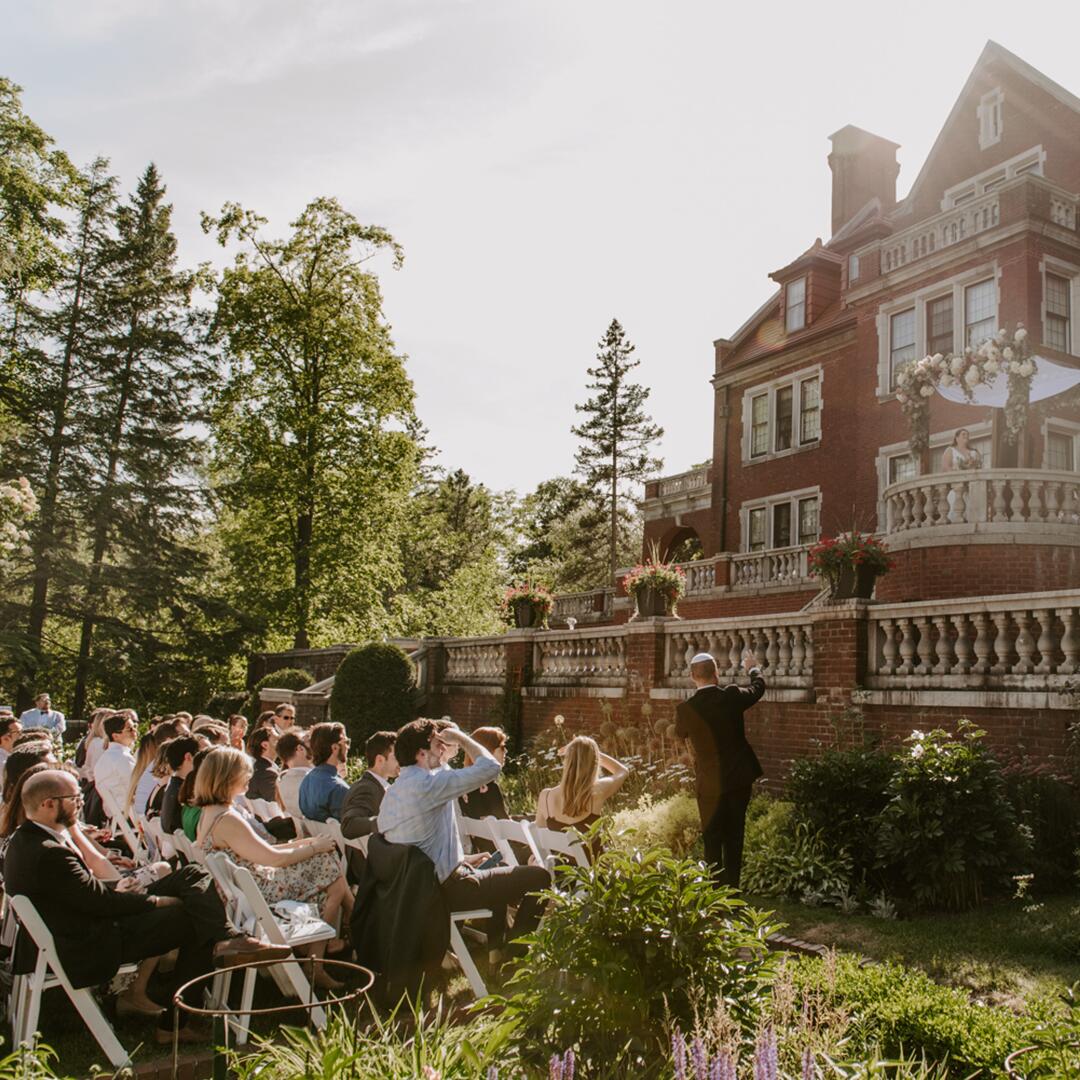 large crowd of seated guests outside on the grass in front of Glensheen, celebrating bride and groom.