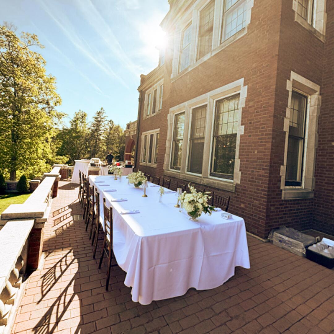 white table cloth long table with flowers set up on the brick patio terrace of Glensheen mansion.