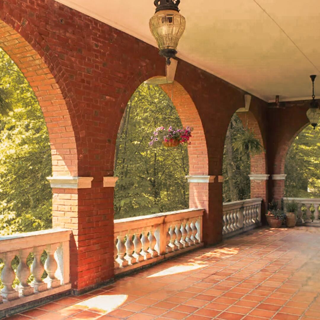 large covered brick patio area with arched walls and hanging flower baskets.
