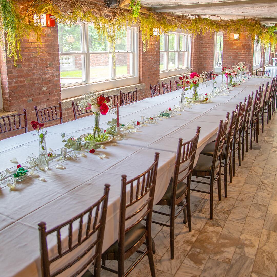 long table with white table cloth, roses, and candles in a brick, long room.