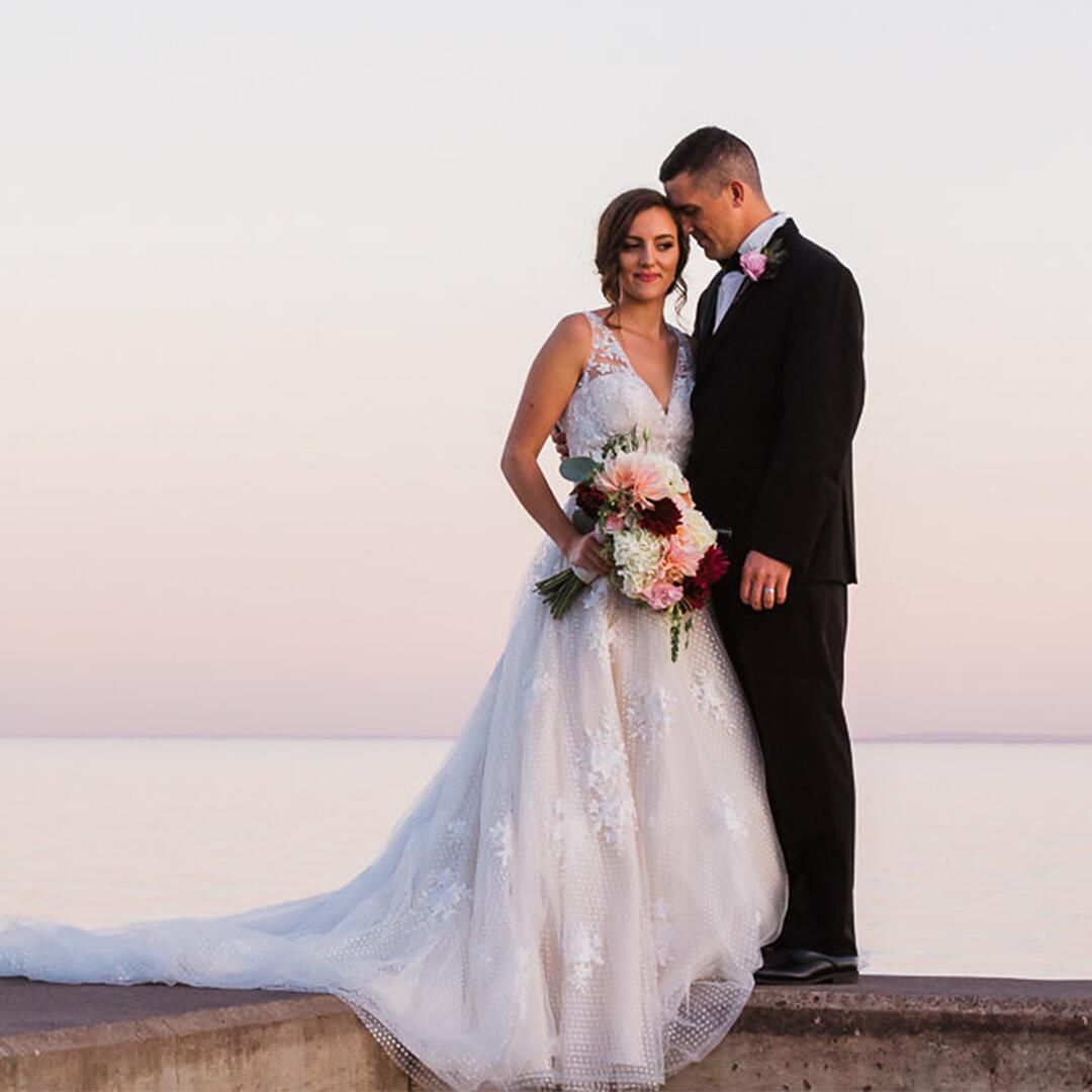 groom with bride holding flowers, standing on concrete platform over lakeview.