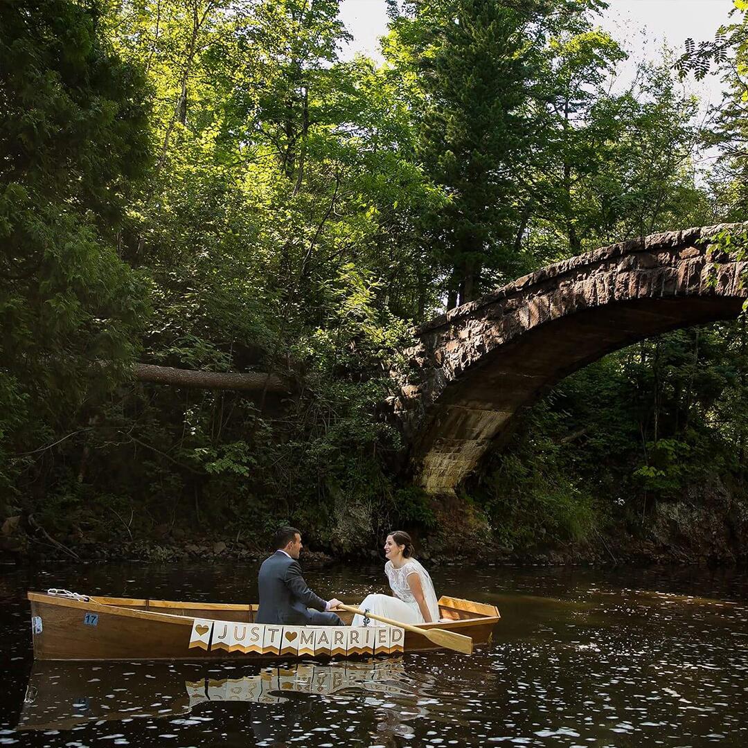 husband and wife on a ‘Just Married’ boat over a stone arch bridge, photo by Derek Montgomery