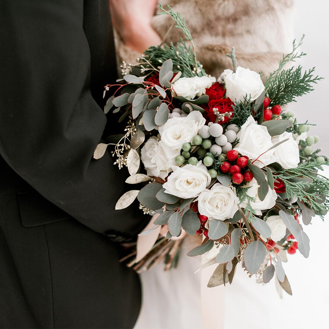 groom and bride holding a white flower bouquet with red berries and greenery.