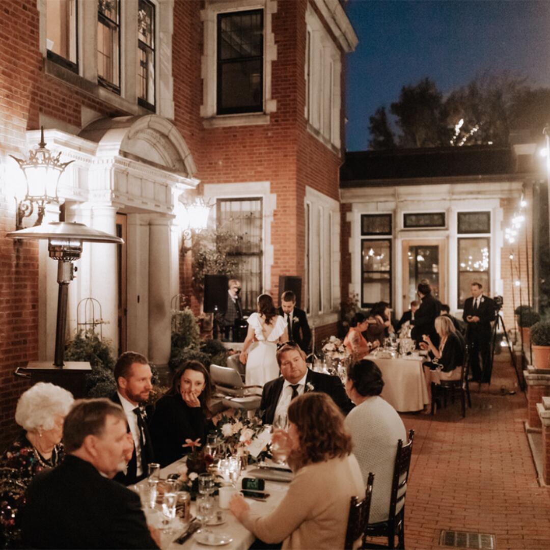 tables of guests eating outside at night on the brick and lit up terrace of Glensheen.