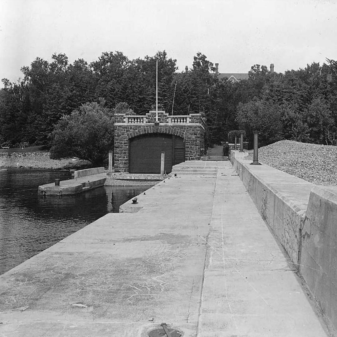 large cement pier over the lake with a brick boathouse in the back.