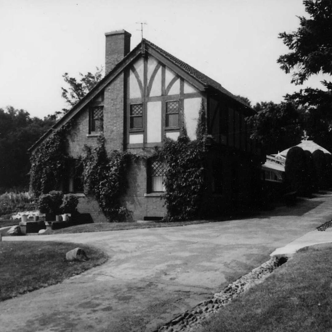 carriage house with a paved path in front and pruned trees surrounding it.