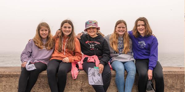 group of five girls smiling and sitting on the ledge of the pier on Lake Superior.