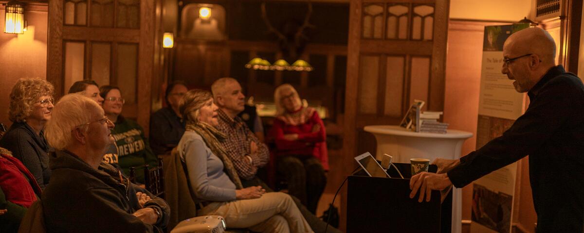 Group of adults seated and listening to a presenting speaker in the Amusement room.
