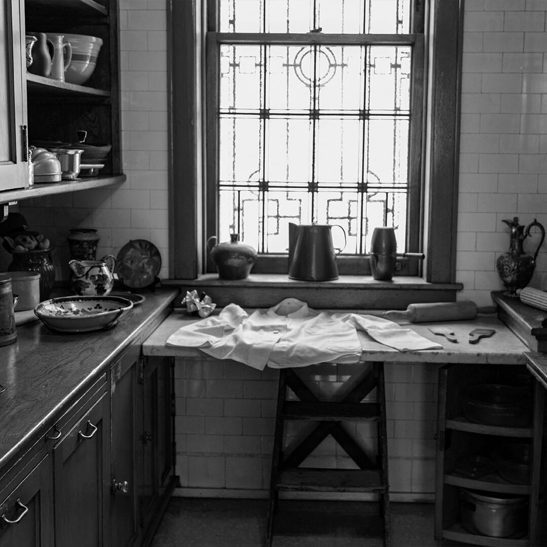 wood pantry counter with shelving and cooking dishware, a shirt and rolling pins layed out in front of a window.