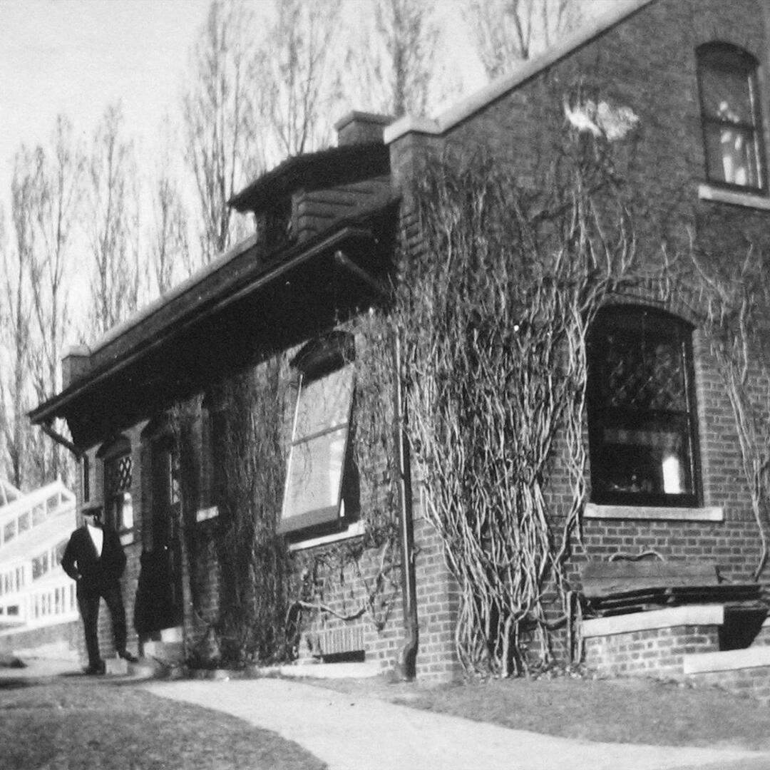 brick gardener's cottage with a paved path to the side and a man standing next to it.