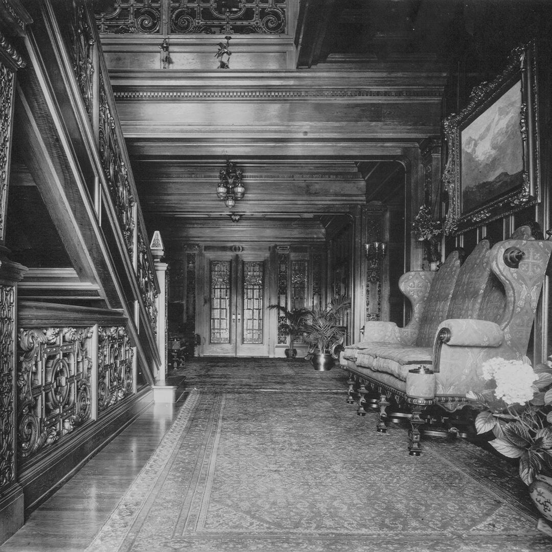 long ornate rug and sofa along a wood paneled wall and wooden stair railing to the left of the front entrance.
