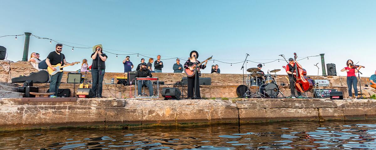 a group of musicians playing instruments and performing on the concrete pier in the lake.
