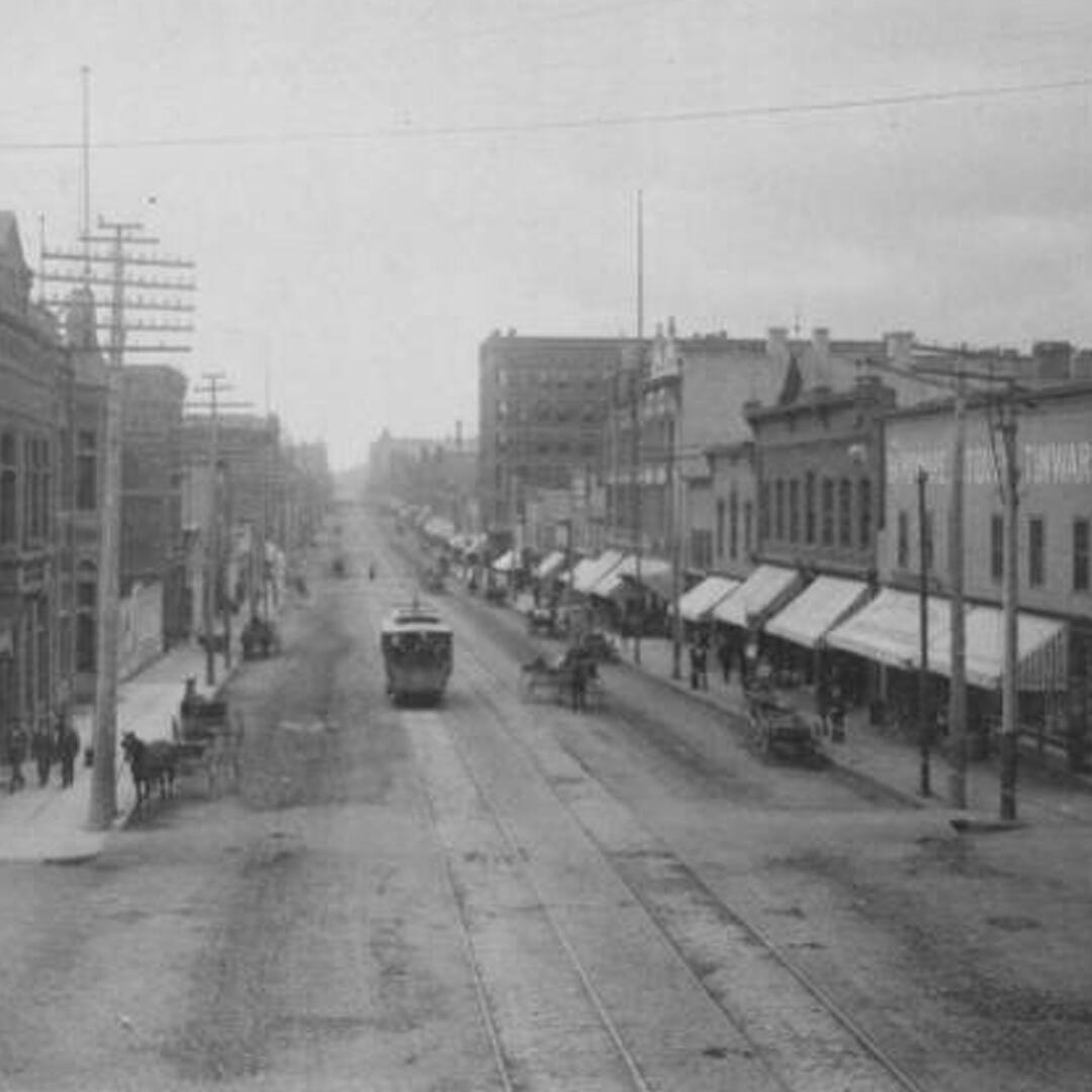 Old street buildings lined up and a trolley going by, early 1900s Superior Street in Duluth, MN.