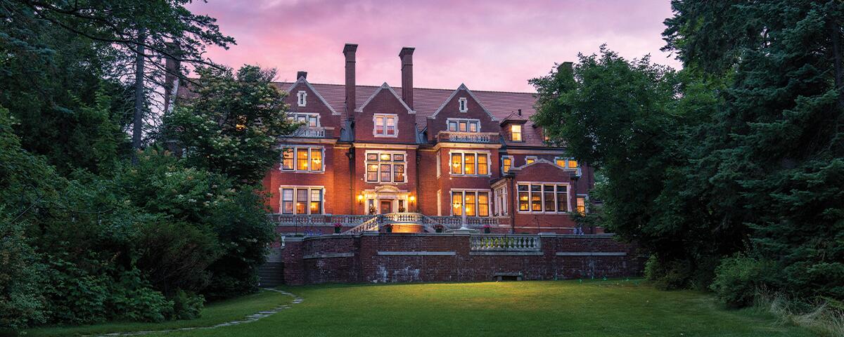 large brick mansion with open lawn in front, trees to the sides, and a pink sunset in the background. Photo by Duluth Visuals.