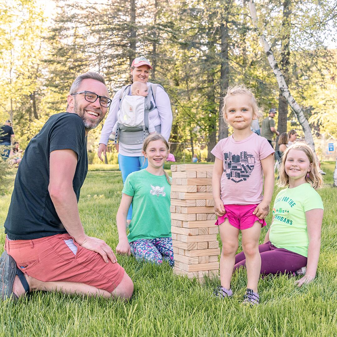 family of five playing jenga on the lawn.