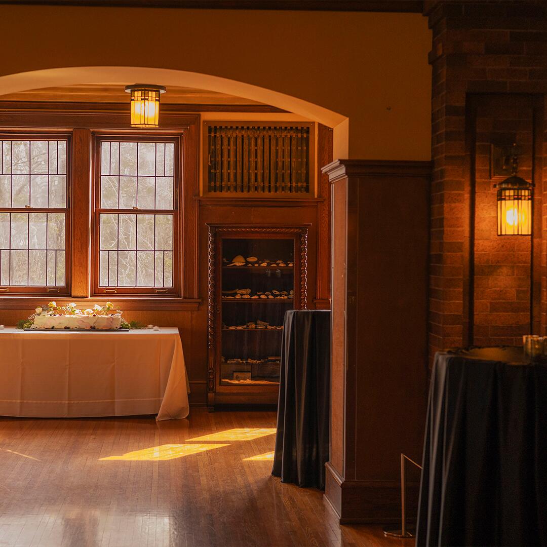 table with floral cake in room with wood floors, lanterns on walls, wood walls with windows.