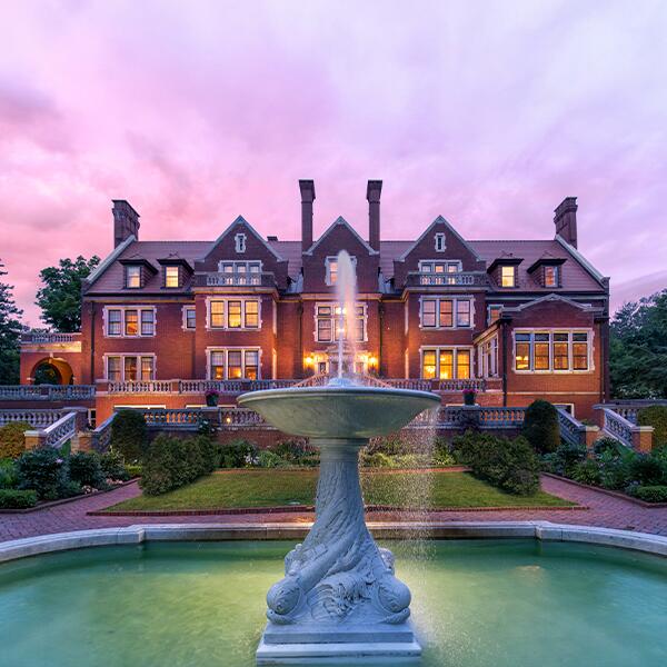 brick exterior of Glensheen with fountain and pink sunset sky behind.