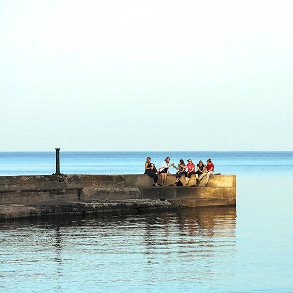 Group of women sitting on the pier and clinking beer cans in celebration
