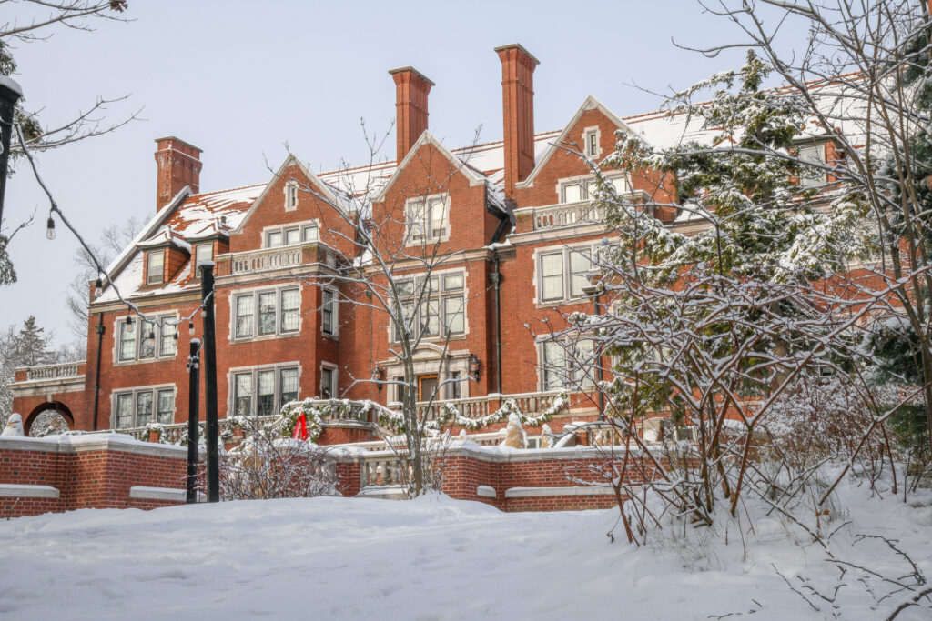 A red brick mansion stands in front of a white, snowy landscape with trees on the right side.