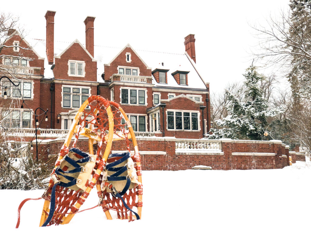 Wooden snowshoes stand in front of a red brick mansion in a pile of white snow.