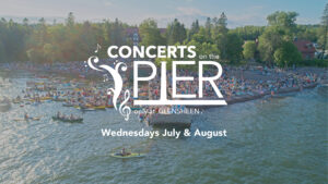 Concerts on the Pier - Only at Glensheen. Water and shoreline with spectators lining a rocky beach and in the water on kayaks and boats.