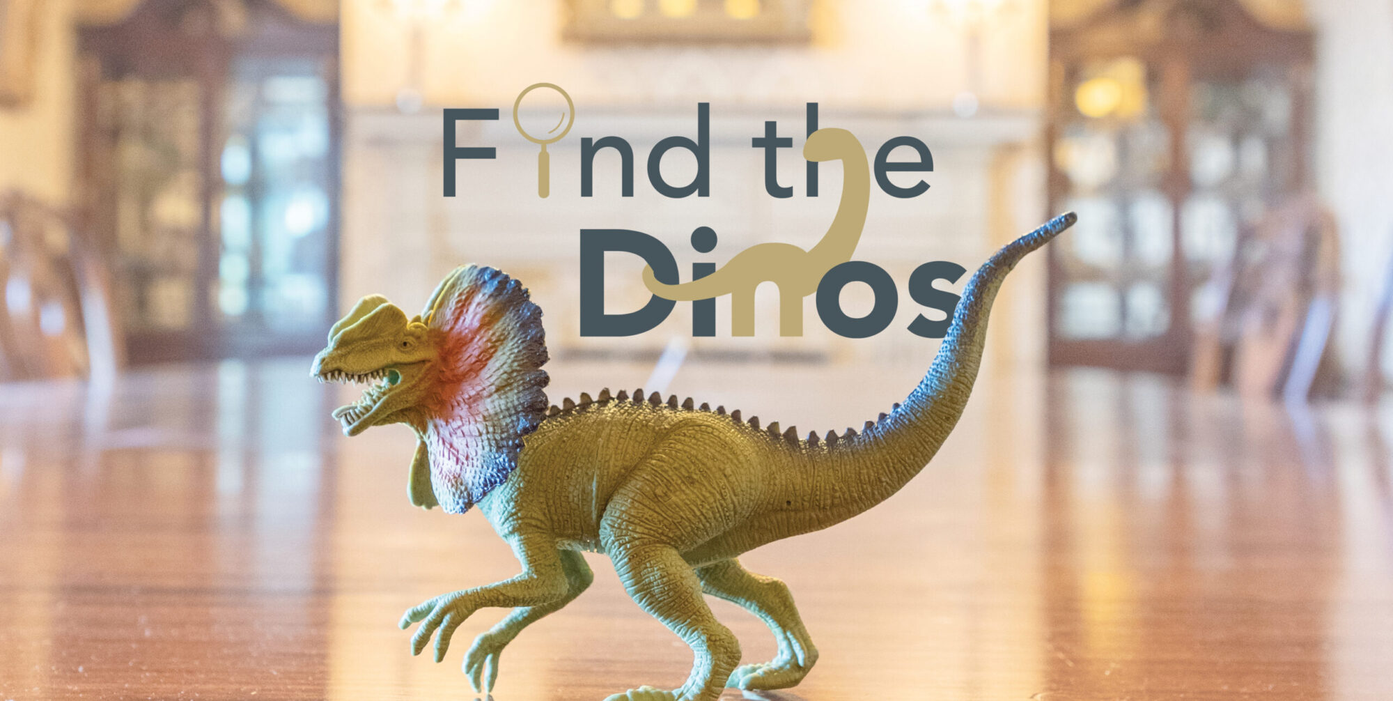 A dinosaur toy sits on a wooden table with the text "Find the dinos".
